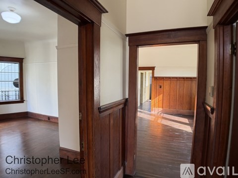 A room with wooden floors and white walls, with a doorway leading to another room.
