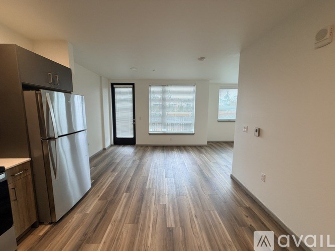 A spacious room with wooden flooring and a refrigerator on the left side.