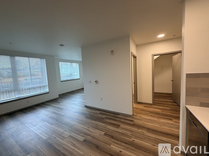 A spacious room with wooden flooring and a large window with blinds.