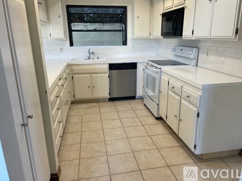 A kitchen with white cabinets and appliances, a window above the sink, and a tiled floor.