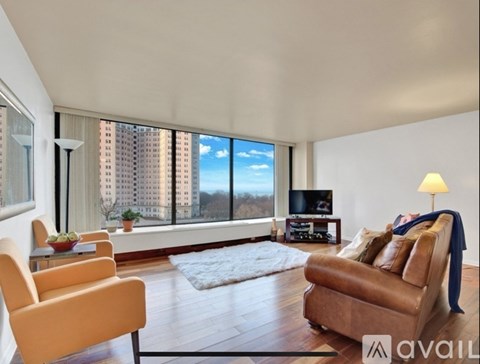 A living room with a brown leather couch and a large window with a view of a building.
