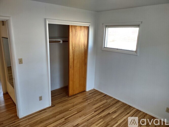 A room with a wooden floor and a white wall with a door and a window.
