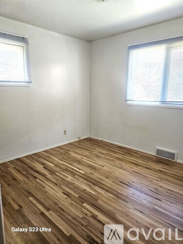 A room with wooden flooring and two windows.