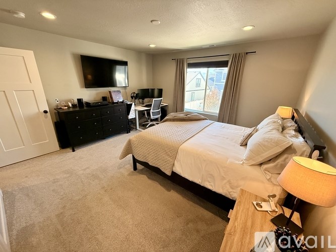 A bedroom with a large bed, a desk with a computer, and a flat-screen TV mounted on the wall.