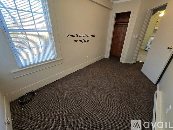 A small bedroom or office with a carpeted floor and a window with blinds.