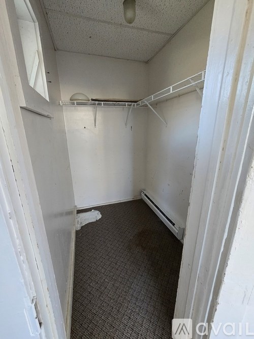 A small, empty room with a carpeted floor and a metal shelf.