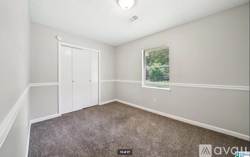 A room with a carpeted floor, a door, a window, and a picture on the wall.