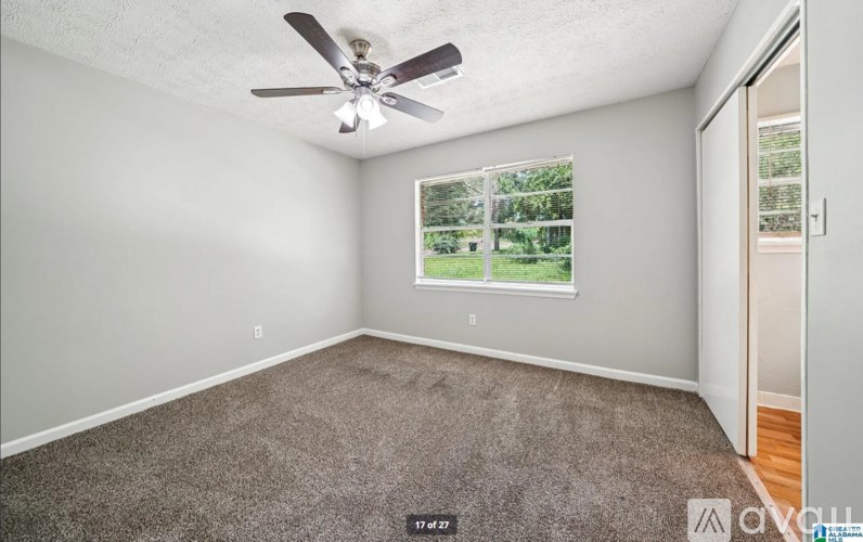 A room with a ceiling fan and a window overlooking a green area.