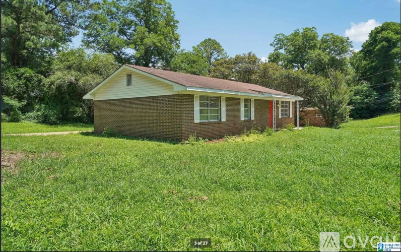 A small house with a red roof is surrounded by green grass and trees.