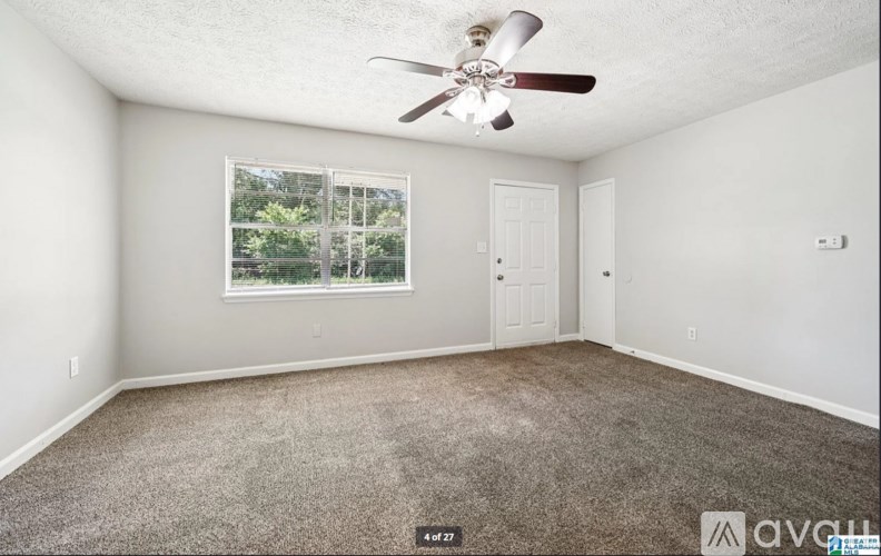 A room with a ceiling fan and a window with a view of trees.