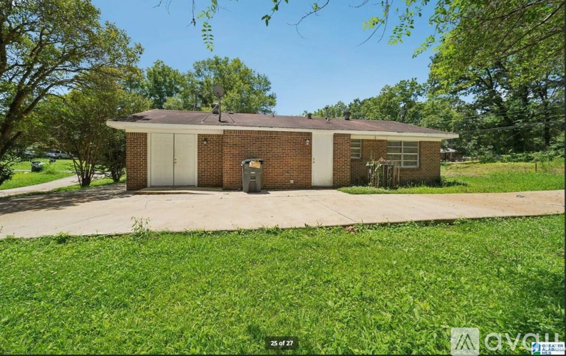 A small brick building with a white door and windows is surrounded by a grassy area.