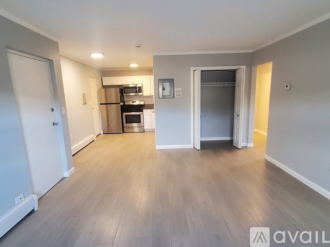 A spacious room with wooden flooring and a kitchen area in the background.