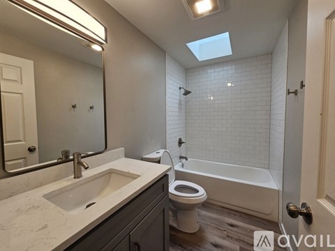 A bathroom with a skylight, a toilet, a sink, and a bathtub.