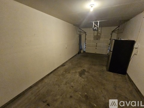 A large empty room with a black refrigerator and a light on the ceiling.