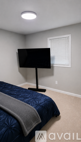 A bedroom with a bed, a television, and a window with blinds.