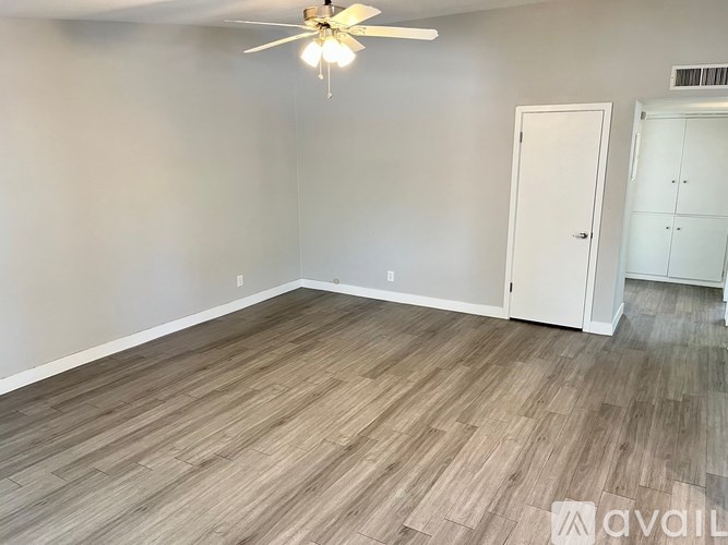 A room with a ceiling fan and light, hardwood flooring, and a white door and cabinet.