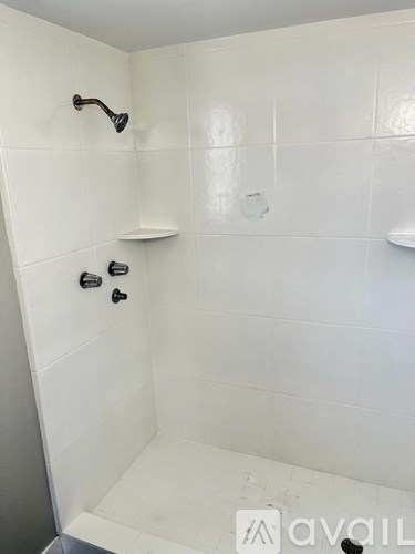 A white tiled shower with a black faucet and a white shelf.
