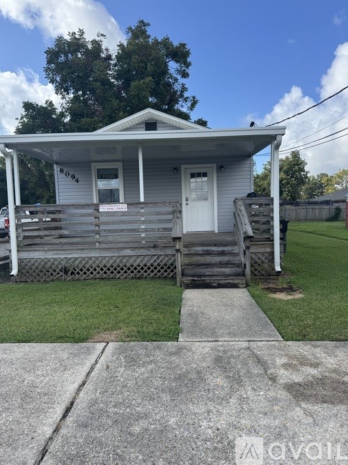 A small white house with a porch and a sign on the front door.