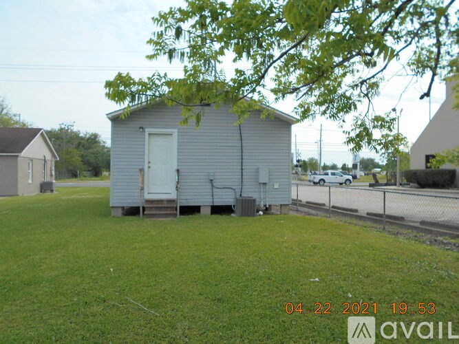 A small grey building with a white door is surrounded by a grassy area.