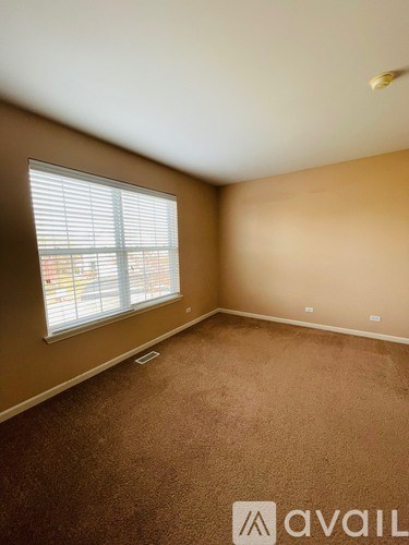A room with a carpeted floor and a window with blinds.