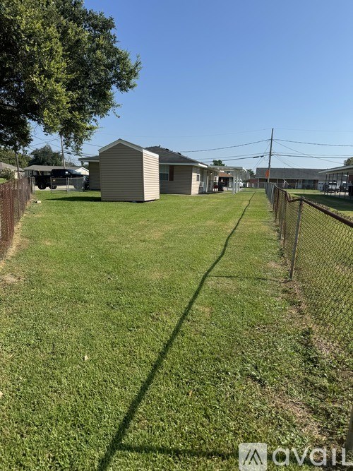 A grassy field with a fence and a few buildings in the background.