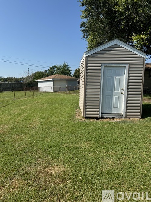 A small grey shed with a blue door is situated in a grassy area.