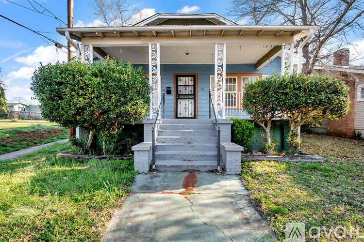 A blue house with a white porch and a green bush.