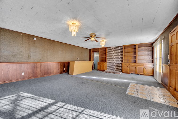 A spacious room with a ceiling fan and wooden paneling on the walls.