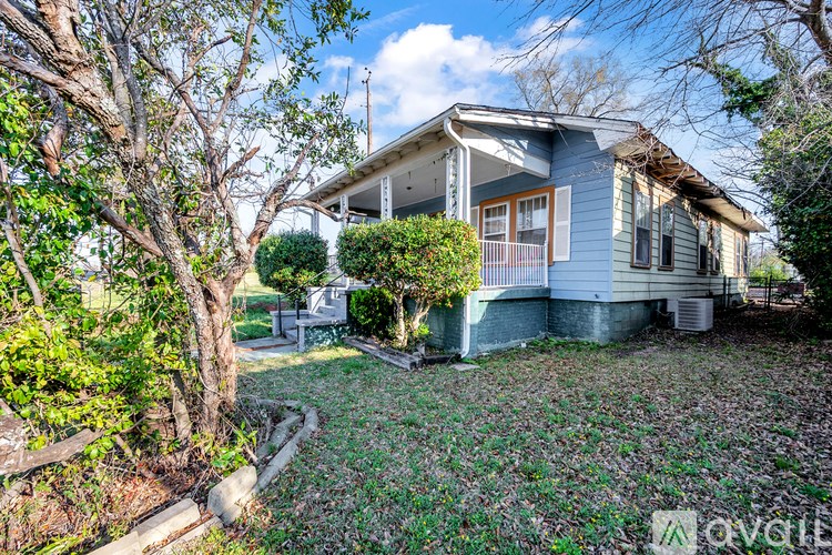 A house with a blue front and a white roof is surrounded by trees and bushes.