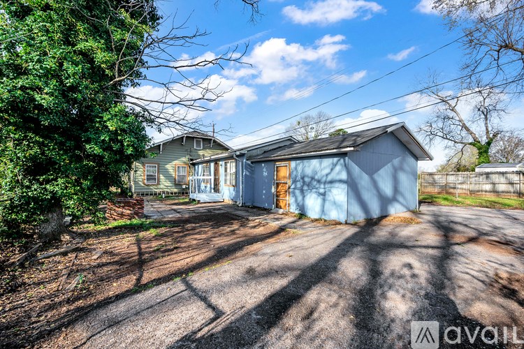 A house with a blue exterior is surrounded by a driveway and greenery.