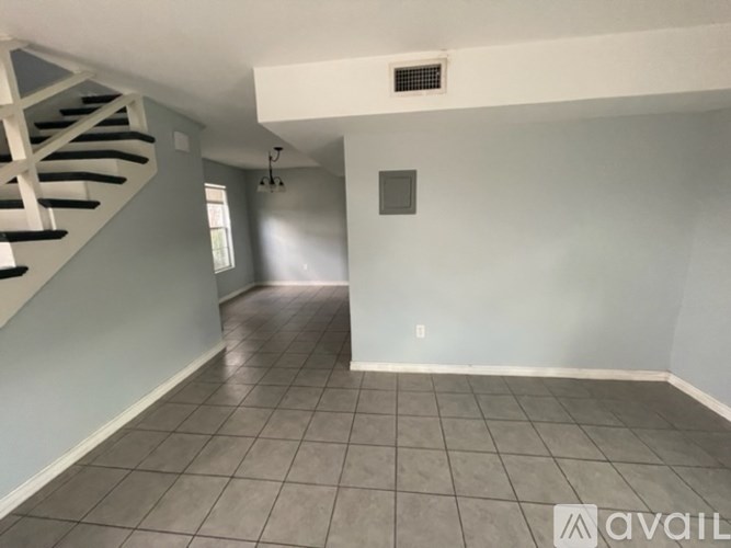 A spacious room with a tiled floor and a staircase on the left side.