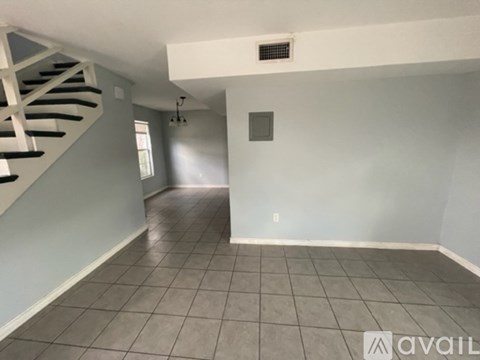 A spacious room with a tiled floor and a staircase on the left side.