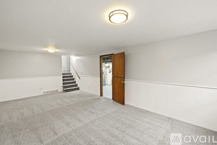 A room with a carpeted floor, a staircase, and a wooden door.