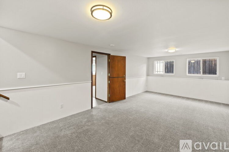 A spacious room with a carpeted floor, a wooden door, and a window with blinds.