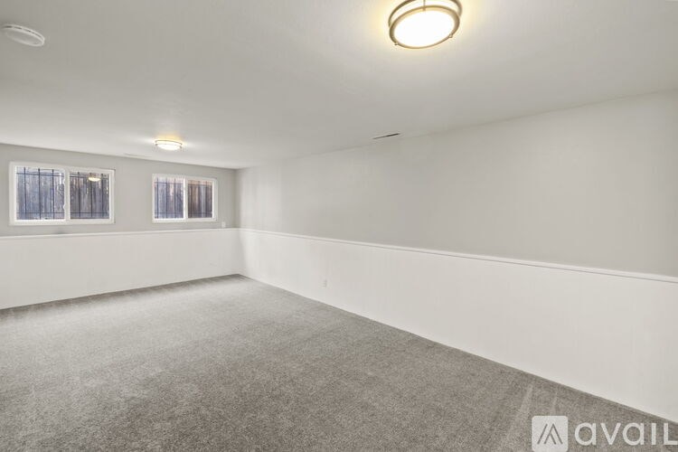 A spacious room with grey carpeting and two windows.