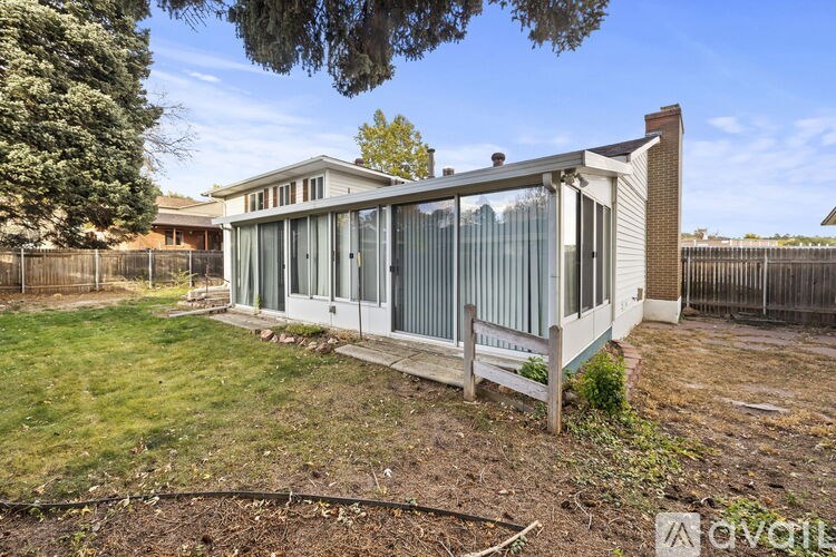 A house with a white exterior and a grey roof is surrounded by a fence and has a small garden in front.