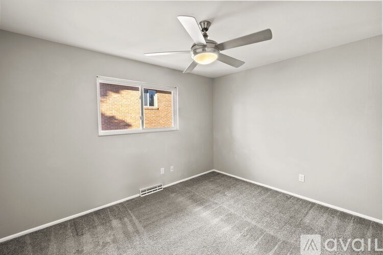A room with a ceiling fan and a window showing a brick wall outside.