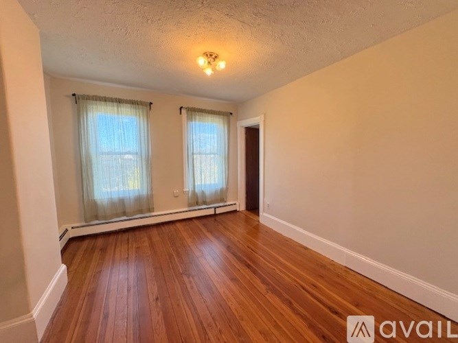 A room with wooden floors and two windows with curtains.