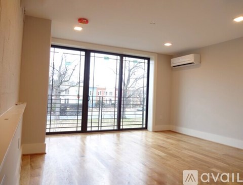 A spacious room with wooden floors and large windows overlooking a parking lot.