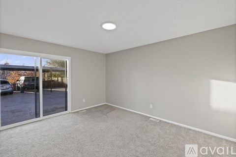 A spacious room with a carpeted floor and a sliding glass door leading to a parking lot.