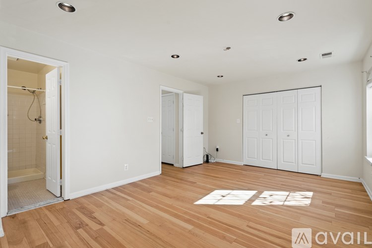 A room with wooden floors and white walls, with a bathroom visible in the background.
