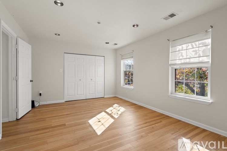 A room with wooden floors and white walls, featuring a large window with a view of trees and a white door.