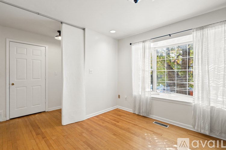 A room with a door, a window with white curtains, and a wooden floor.