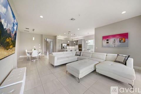 A spacious living room with white furniture and a large painting on the wall.