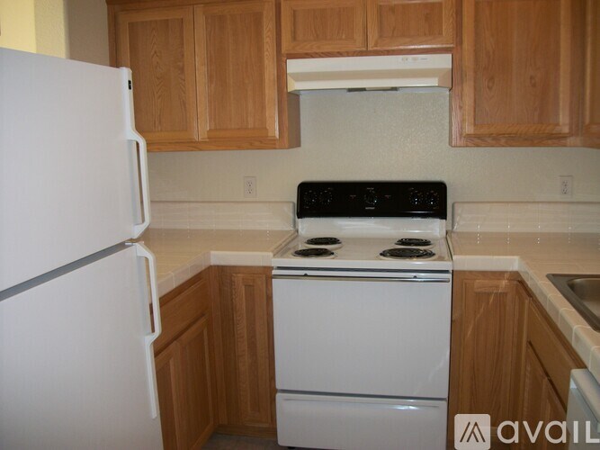 A white refrigerator stands next to a white stove in a kitchen with wooden cabinets.
