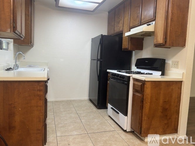 A kitchen with a black refrigerator, white stove, and wooden cabinets.