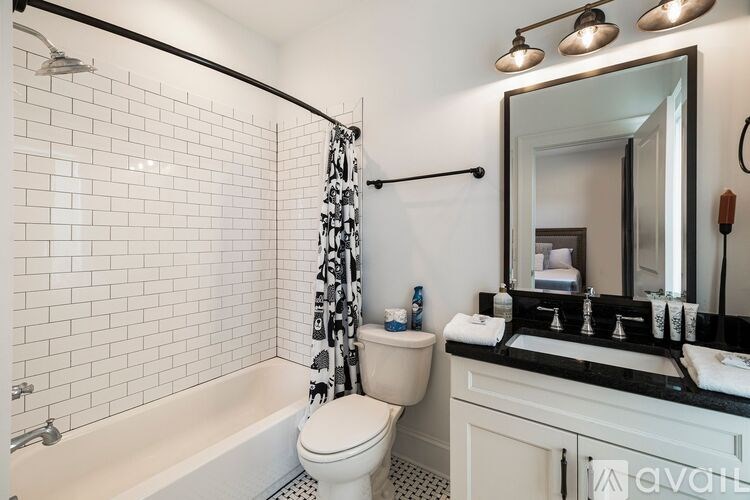 A bathroom with a white toilet, a white bathtub, and a black and white tiled wall.