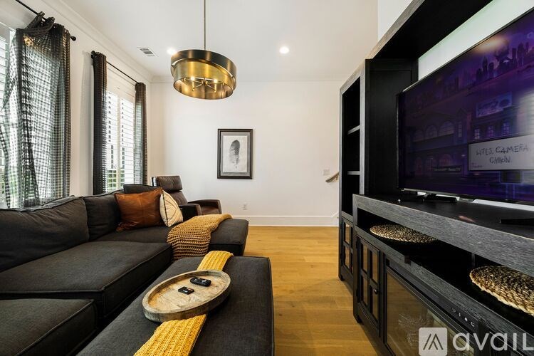 A modern living room with a black couch and a television displaying the words "LITE, CAMERA, GRABBIN".