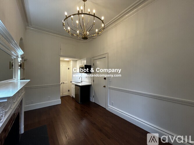 A chandelier hangs from the ceiling in a room with wooden floors and white walls.