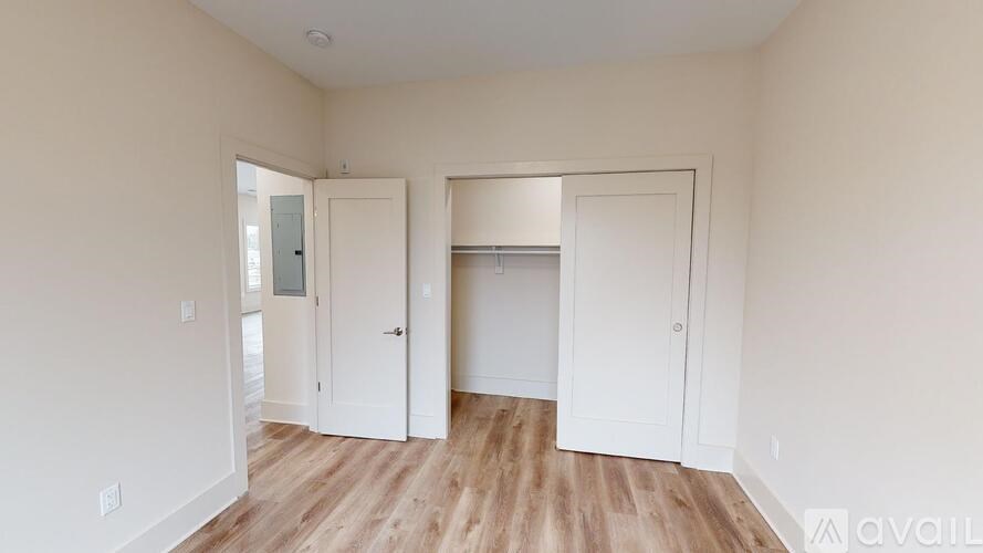 A room with white walls and wooden floors, with two doors open.